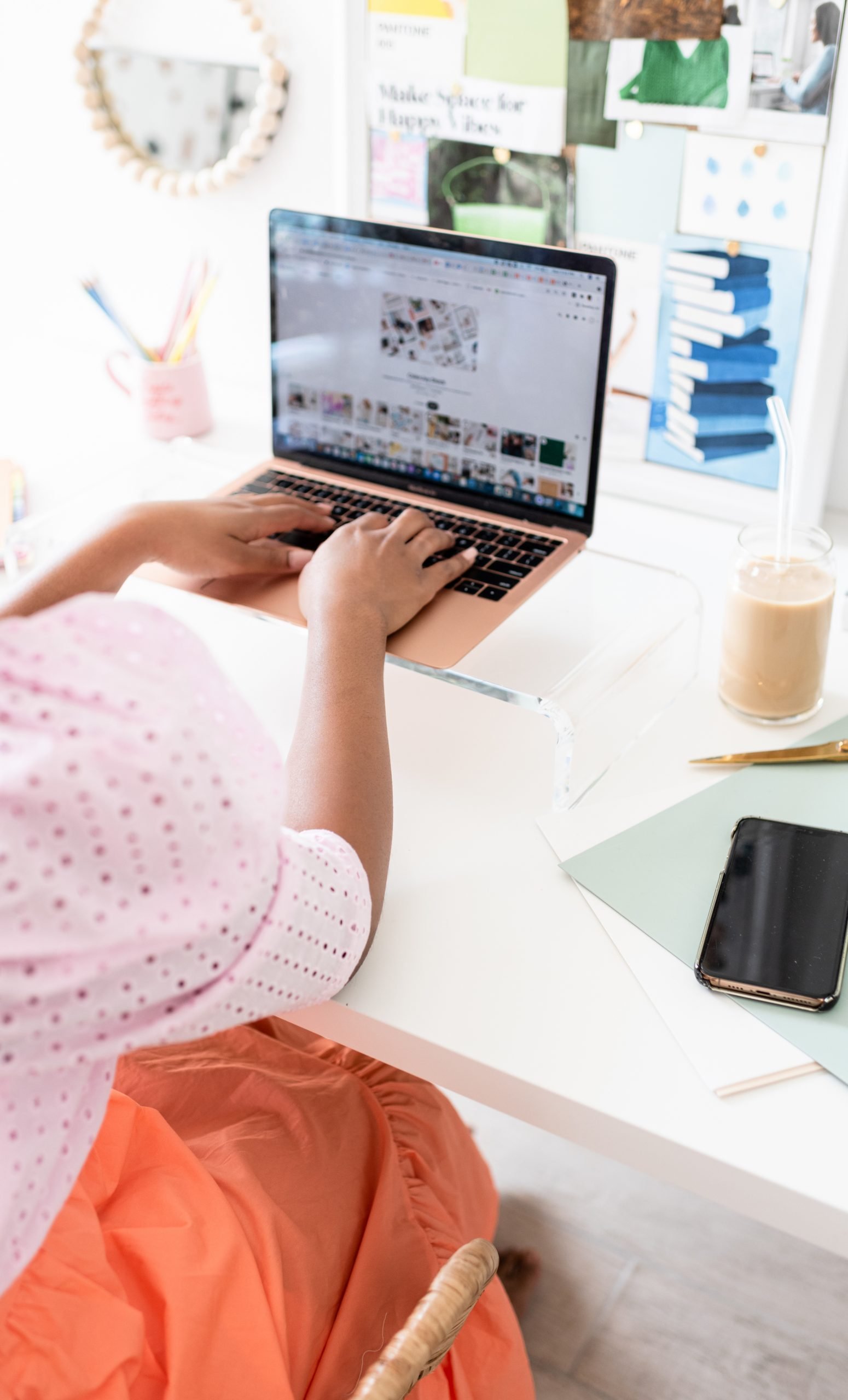 Person typing on a laptop at a desk with a beverage, phone, and stationery items.